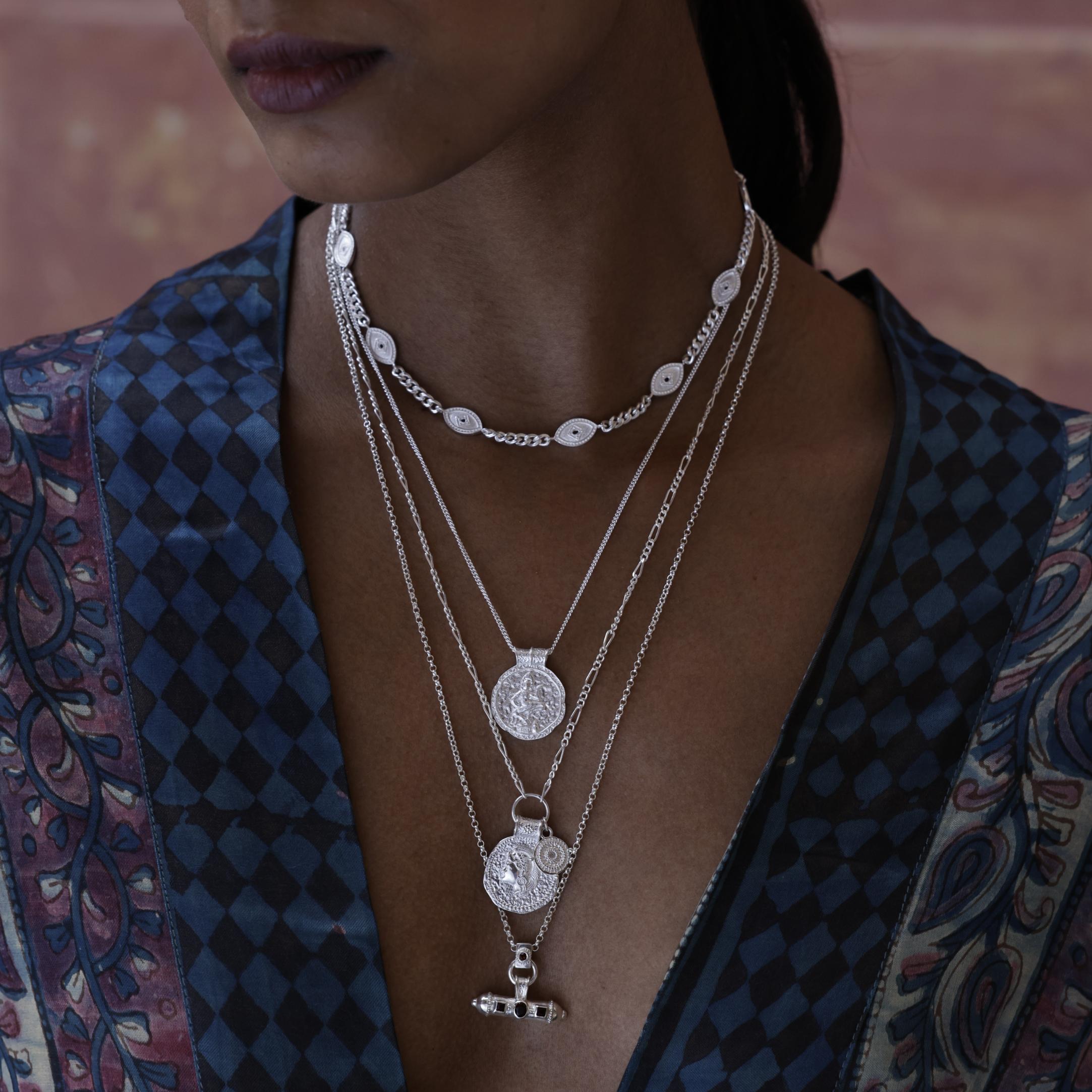 Close-up of a person wearing multiple silver necklaces and talismans with intricate designs.