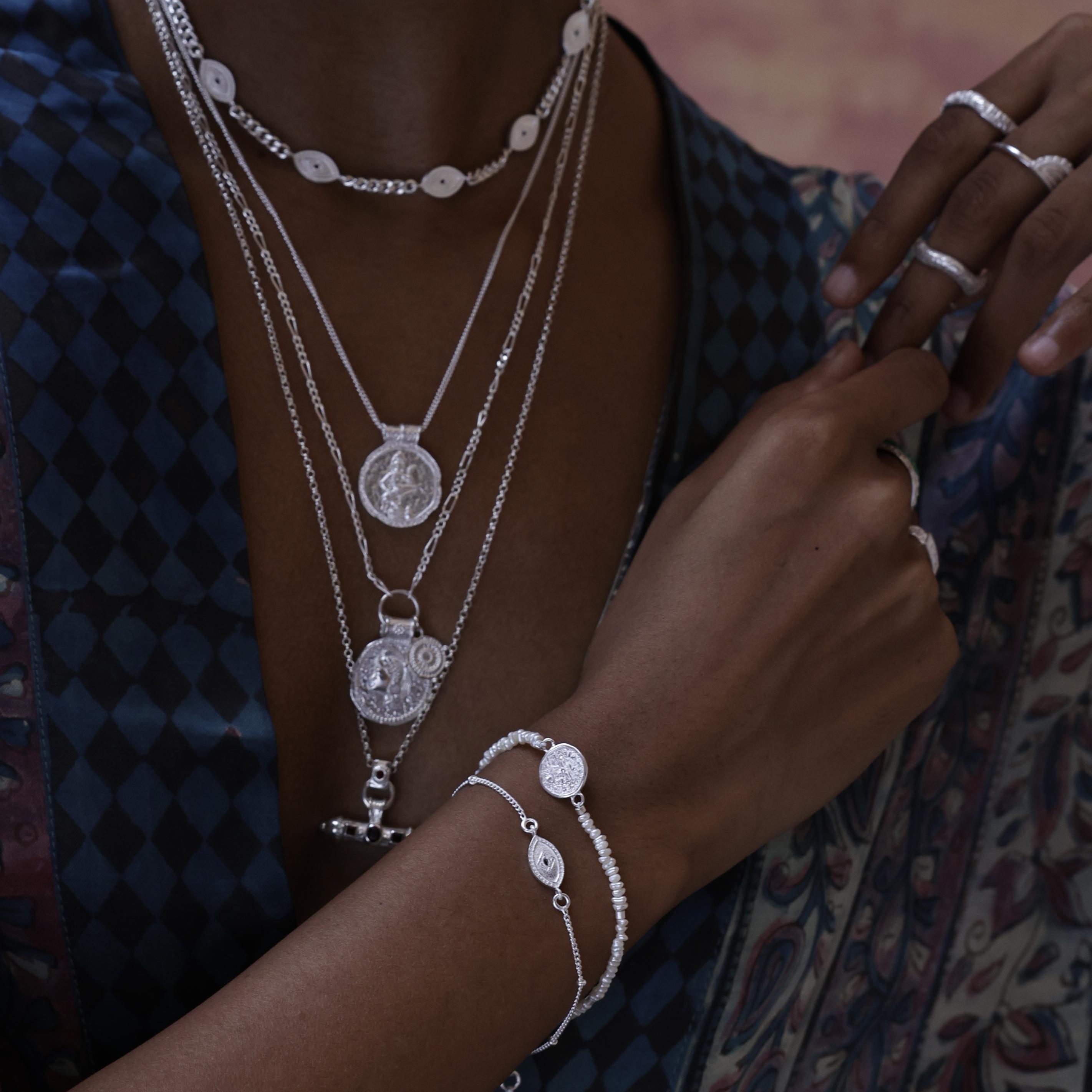 Close-up of a person wearing multiple silver bracelets and talismans designed for everyday layering or gifting with meaning.