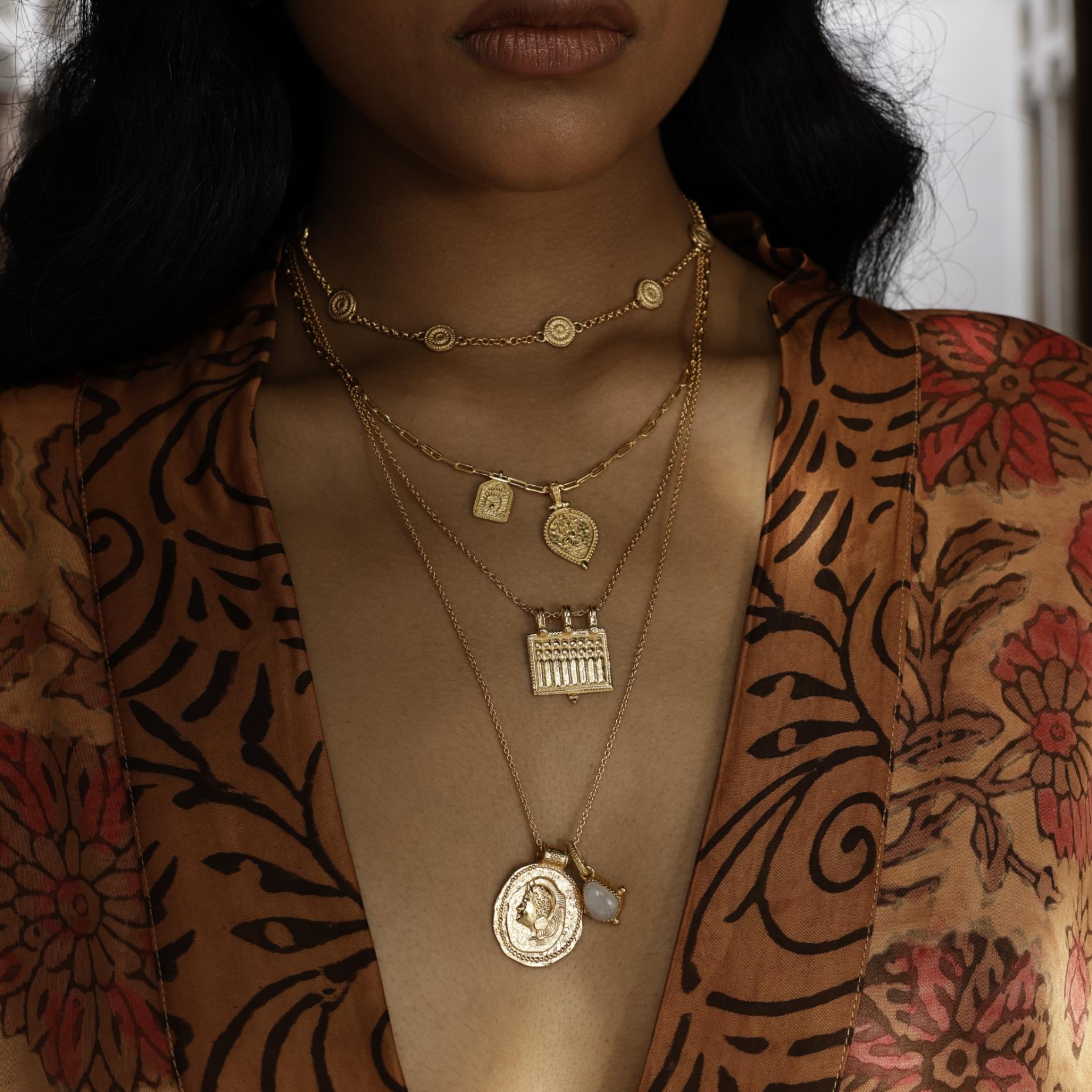 Woman wearing multiple gold necklaces with intricate designs against a patterned kimono