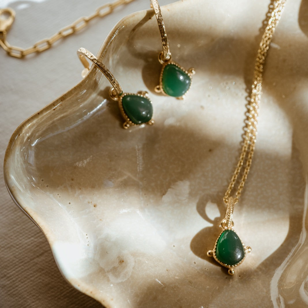 Gold charm necklace and earrings with green stones on a textured surface