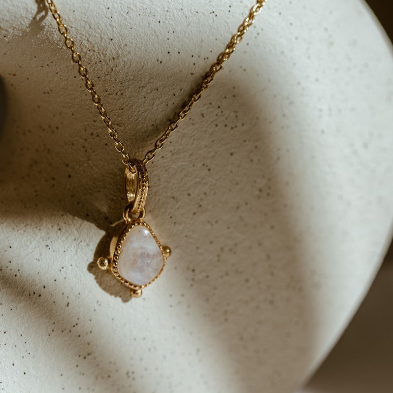 Gold necklace with a moonstone pendant on a textured beige surface