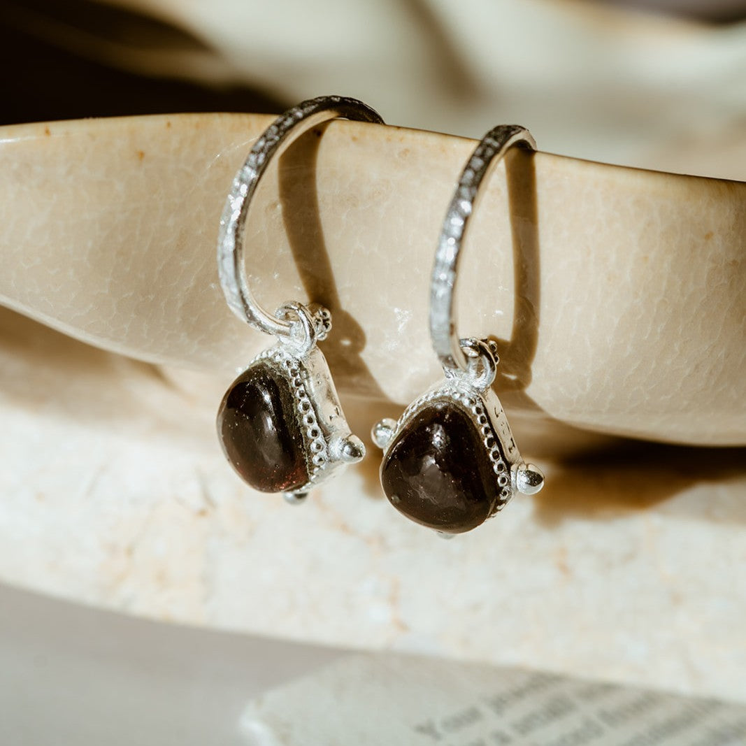 Silver hoops with garnet gemstone on marble background