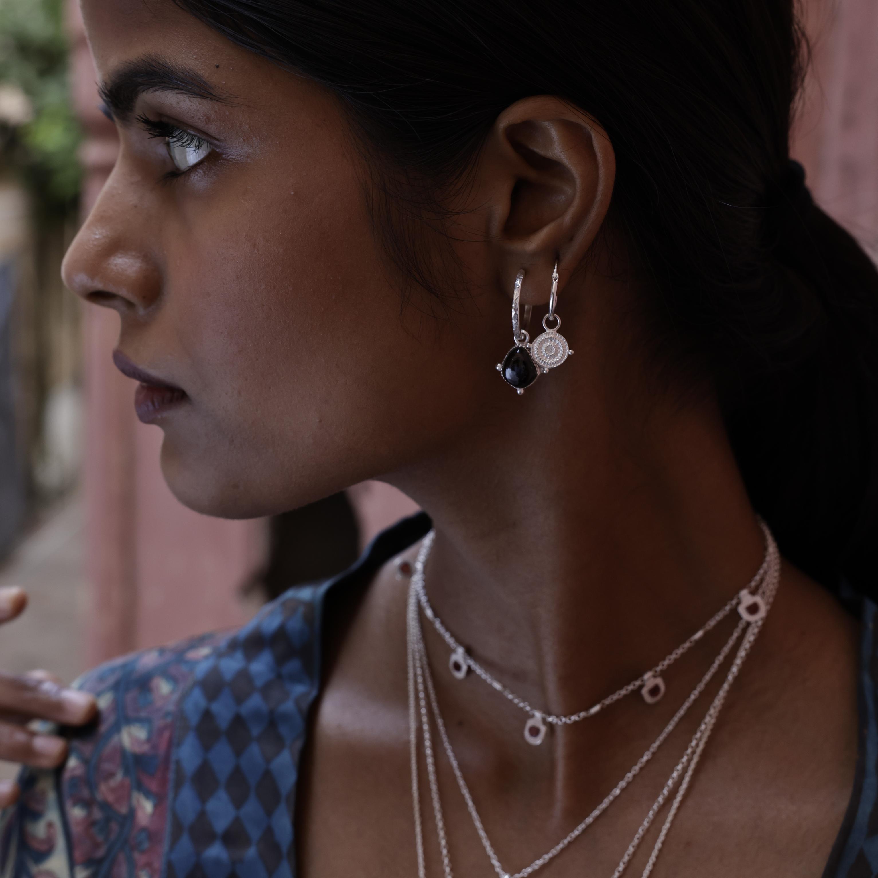 Woman wearing small silver shield hoop earrings layered with other Loft & Daughter talismans