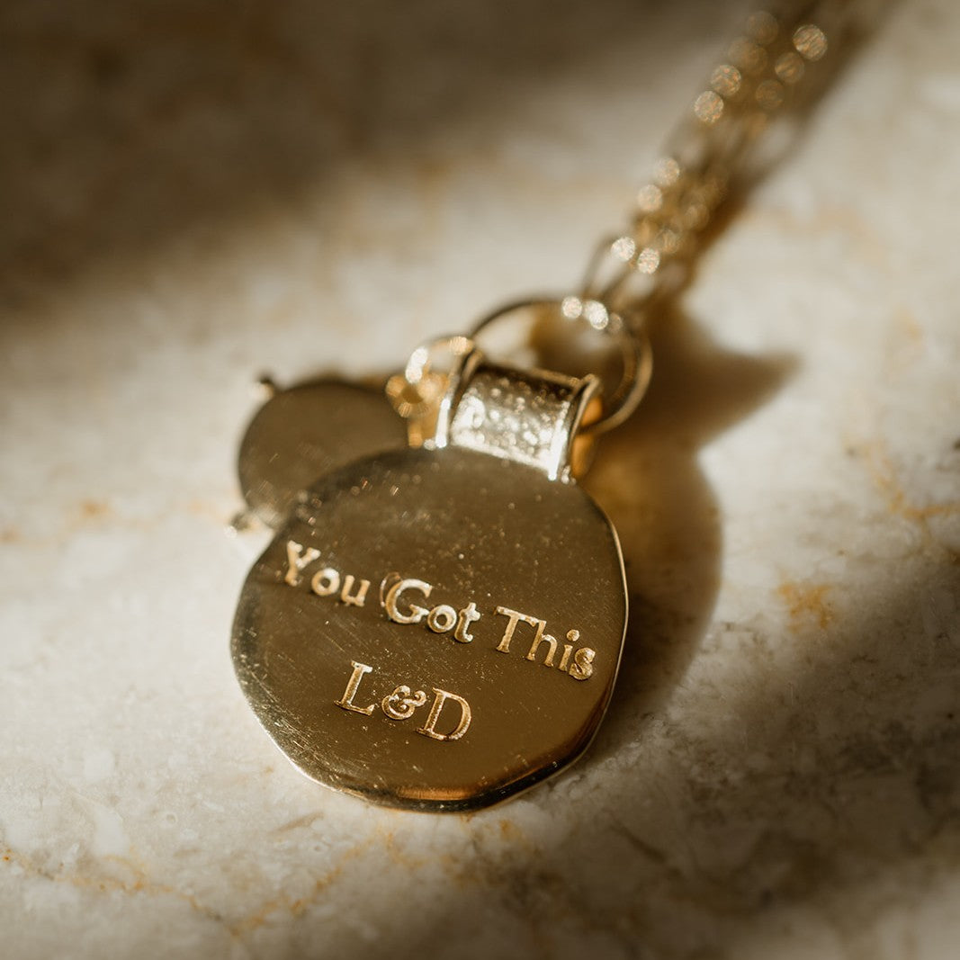 Gold coin necklace with a pendant that says 'You Got This' on a marble surface