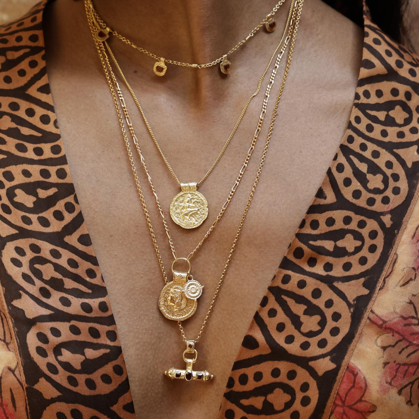 Model wearing the Nivara Amulet garnet necklace stacked with other Loft & Daughter gold coin pendants