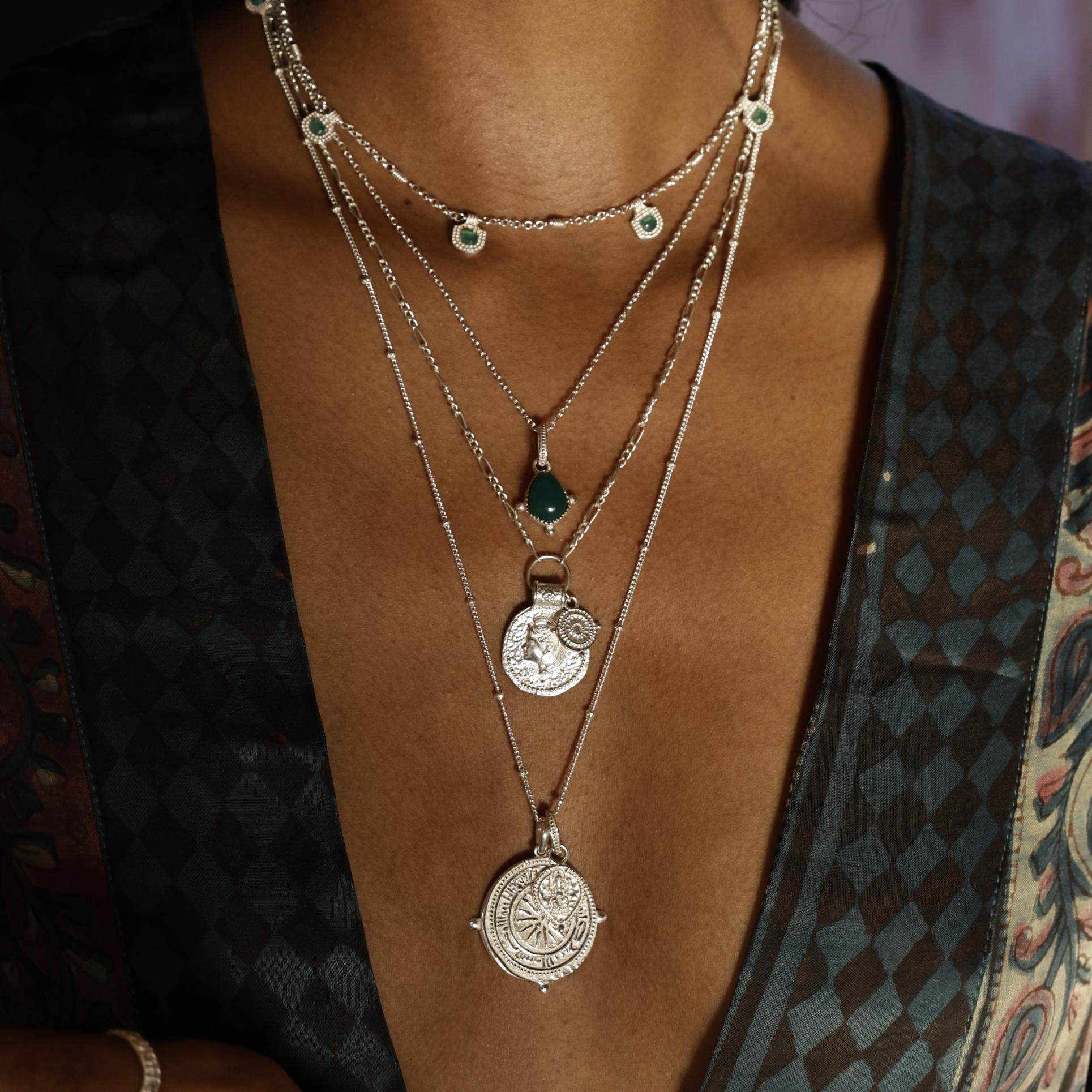 Layered necklaces with coins and green gemstones on a person wearing a patterned kimono