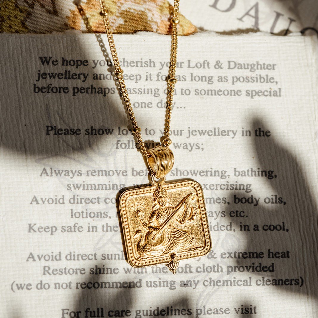Gold Saraswati pendant necklace resting on a jewellery care card