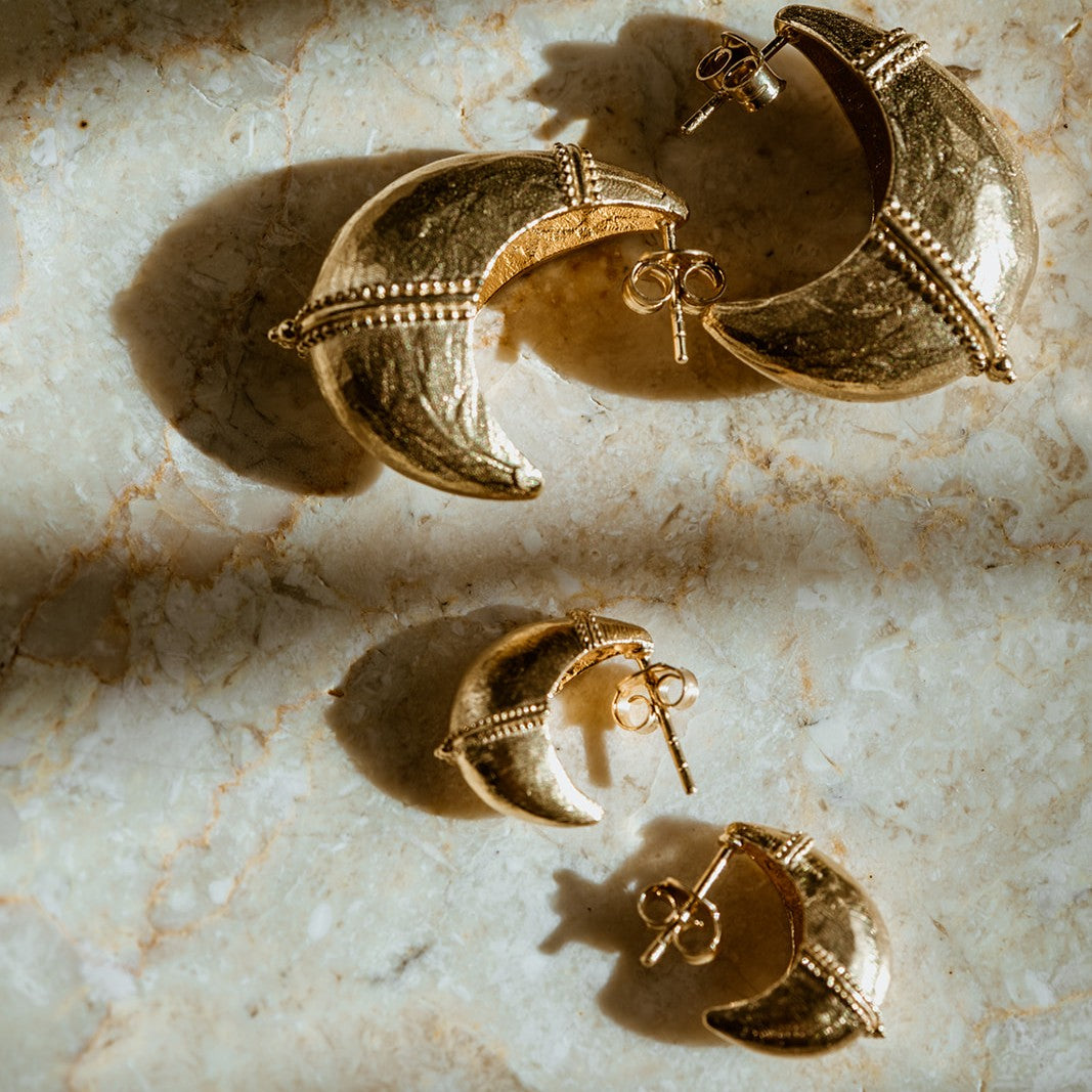 Gold crescent moon-shaped tribal inspired hoop earrings on a marble surface