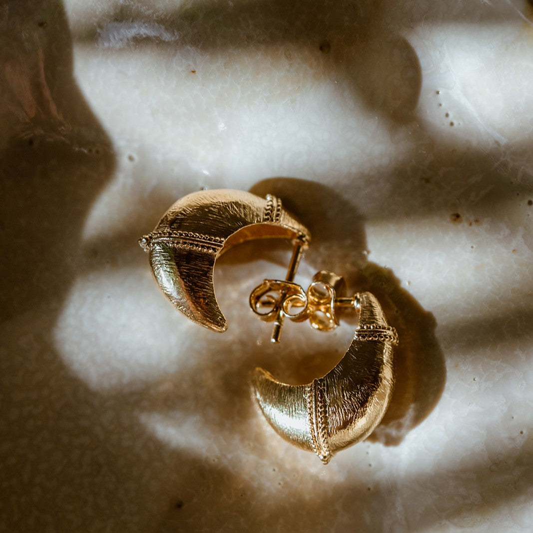 Baby Valora gold dome earrings with subtle hammered surface on marble 
background