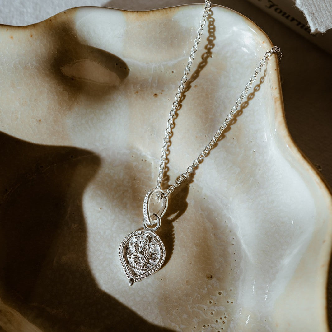 Silver necklace with a decorative surface featuring Lord Ganesh pictured on neutral dish