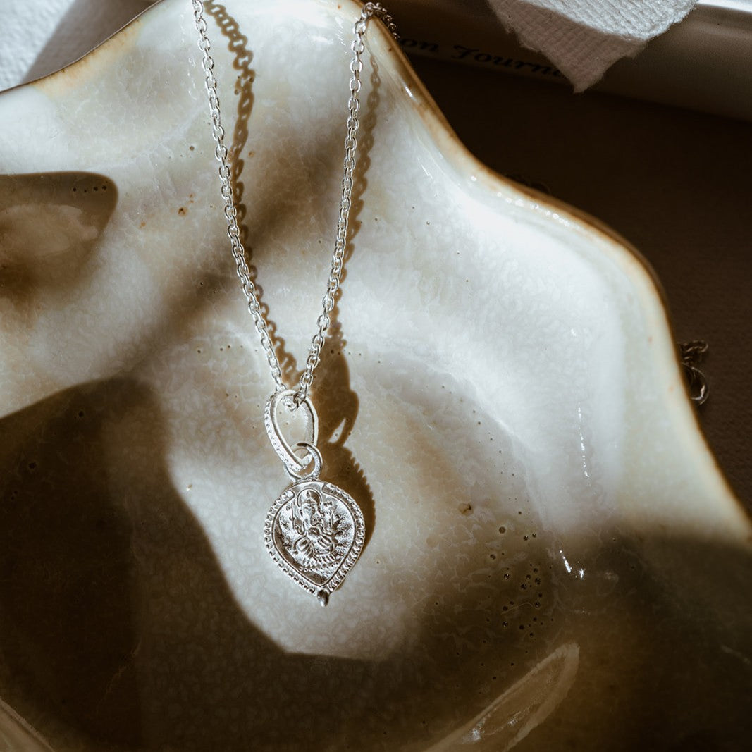Silver Ganesha tear drop necklace on textured surface by Loft & Daughter