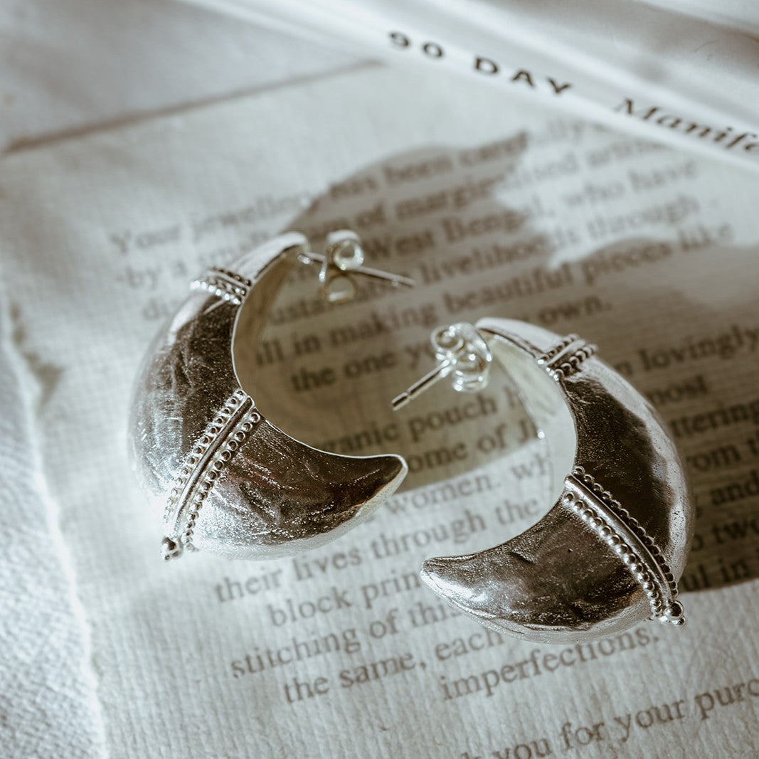 Silver moon-shaped tribal inspired earrings on a piece of paper with text.