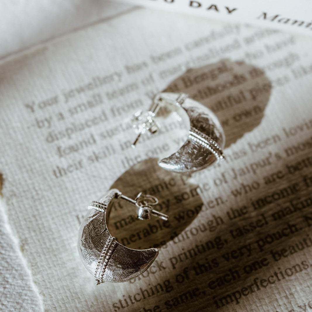 Baby Valora Dome Hoop Earrings in polished silver with softly domed silhouette on a book background