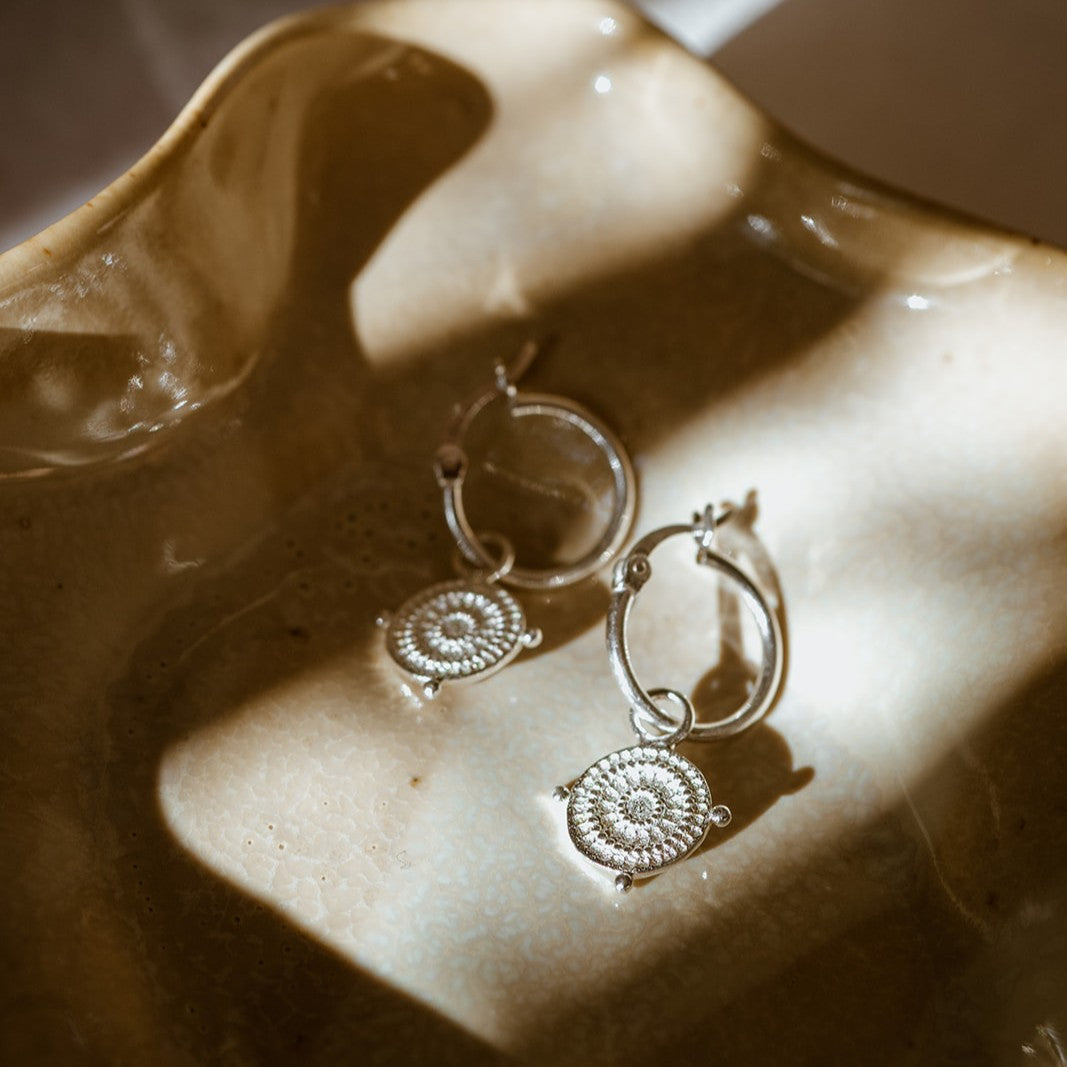 Protective silver shield hoops inspired by Athena’s Aegis, photographed in a beige dish