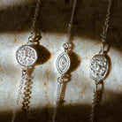 Three dainty silver stacking bracelets featuring small Lakshmi charm, delicate evil eye charm and oval durga coin by Loft & Daughter