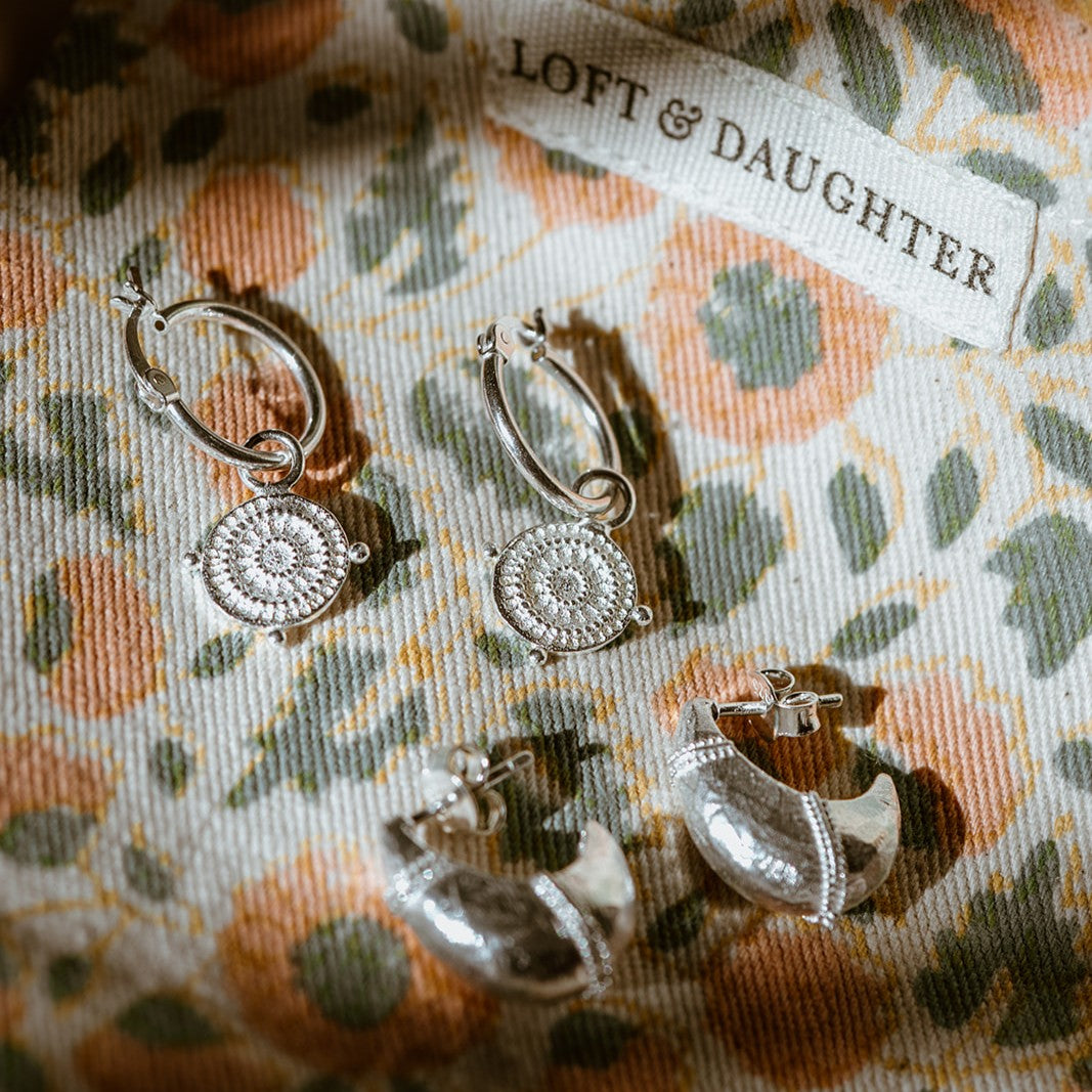 Silver hoop shield earrings on a floral fabric with 'LOFT & DAUGHTER' label.
