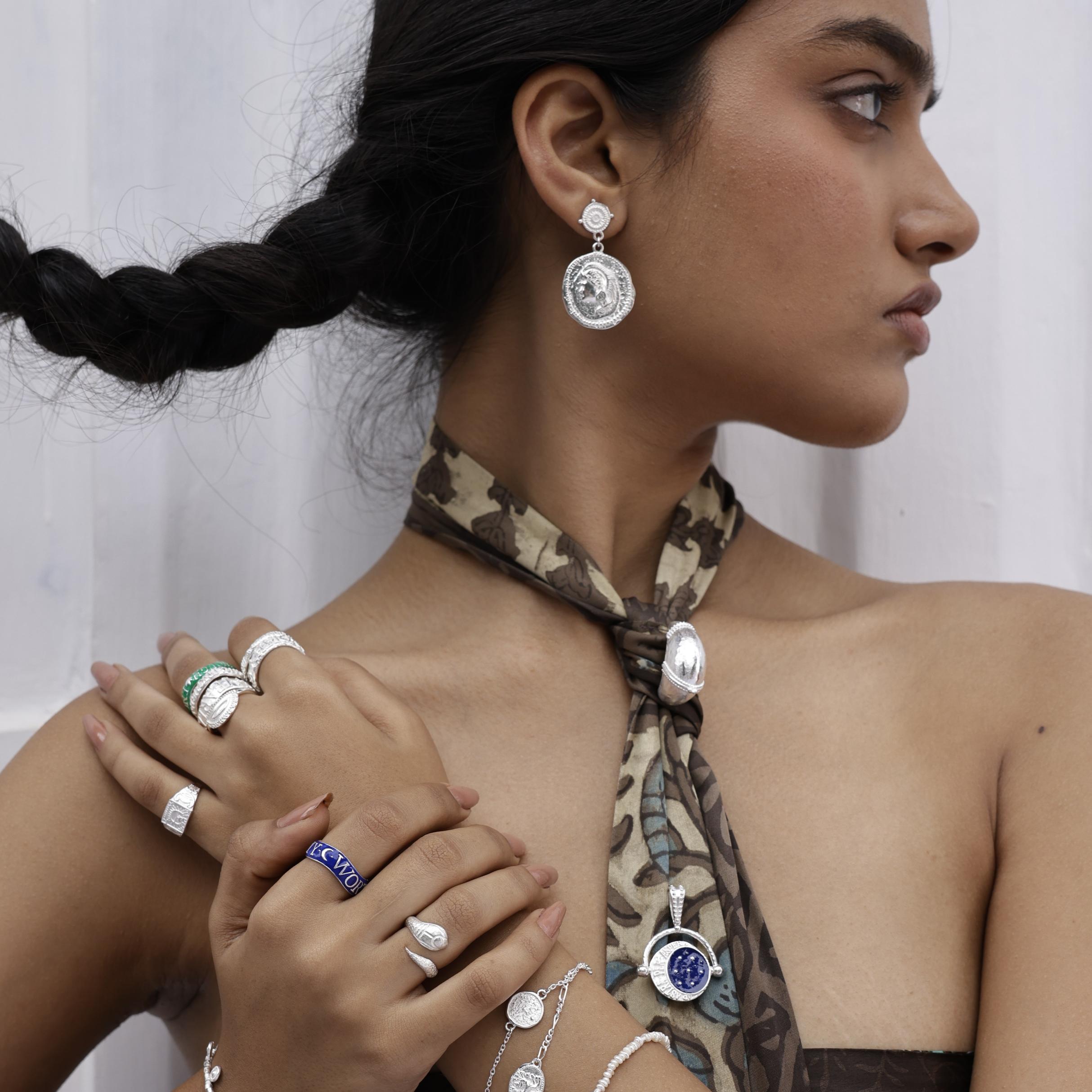 Woman wearing bohemian silver earrings, rings, and a necklace with a plain background by Loft & Daughter