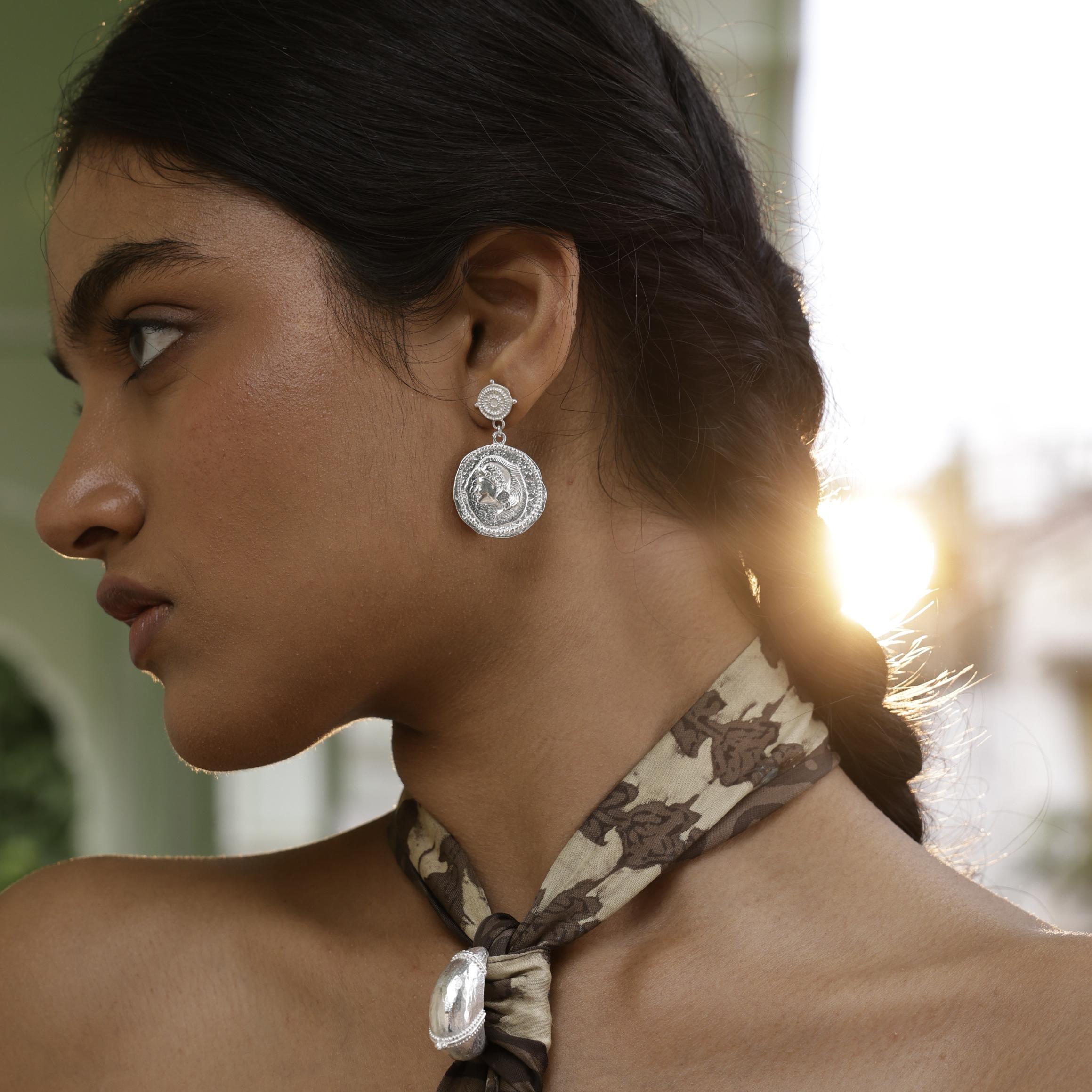 Woman wearing silver Loft & Daughter Athena Coin earrings with a blurred background