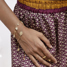 Gold vermeil Durga stacking bracelet with boho coin bracelet worn by model with patterned trousers.
