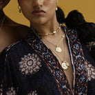 Close-up of a person wearing gold necklaces with a patterned garment against a yellow background  by Loft & Daughter featuring Ganesh and Athena