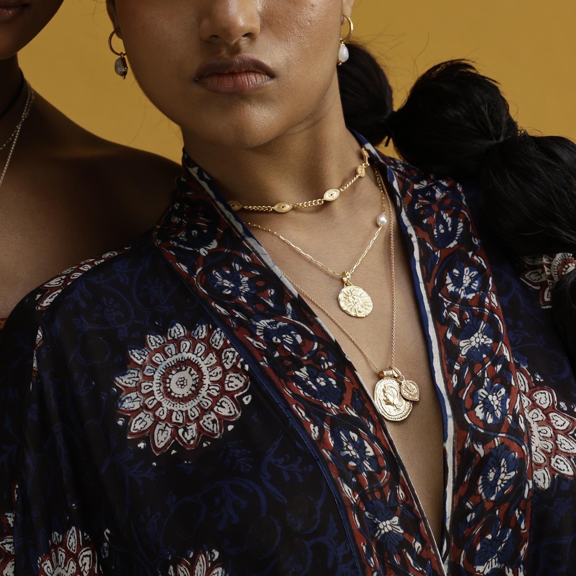 Close-up of a person wearing gold necklaces with a patterned garment against a yellow background  by Loft & Daughter featuring Ganesh and Athena
