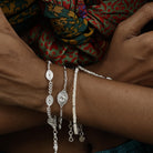 Close up of model wearing delicate silver stacking bracelets featuring evil eye charms and an oval Durga charm, worn with dainty pearl braclet.
