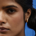 Close-up of a person wearing a gold dome hoop earring with a blue background