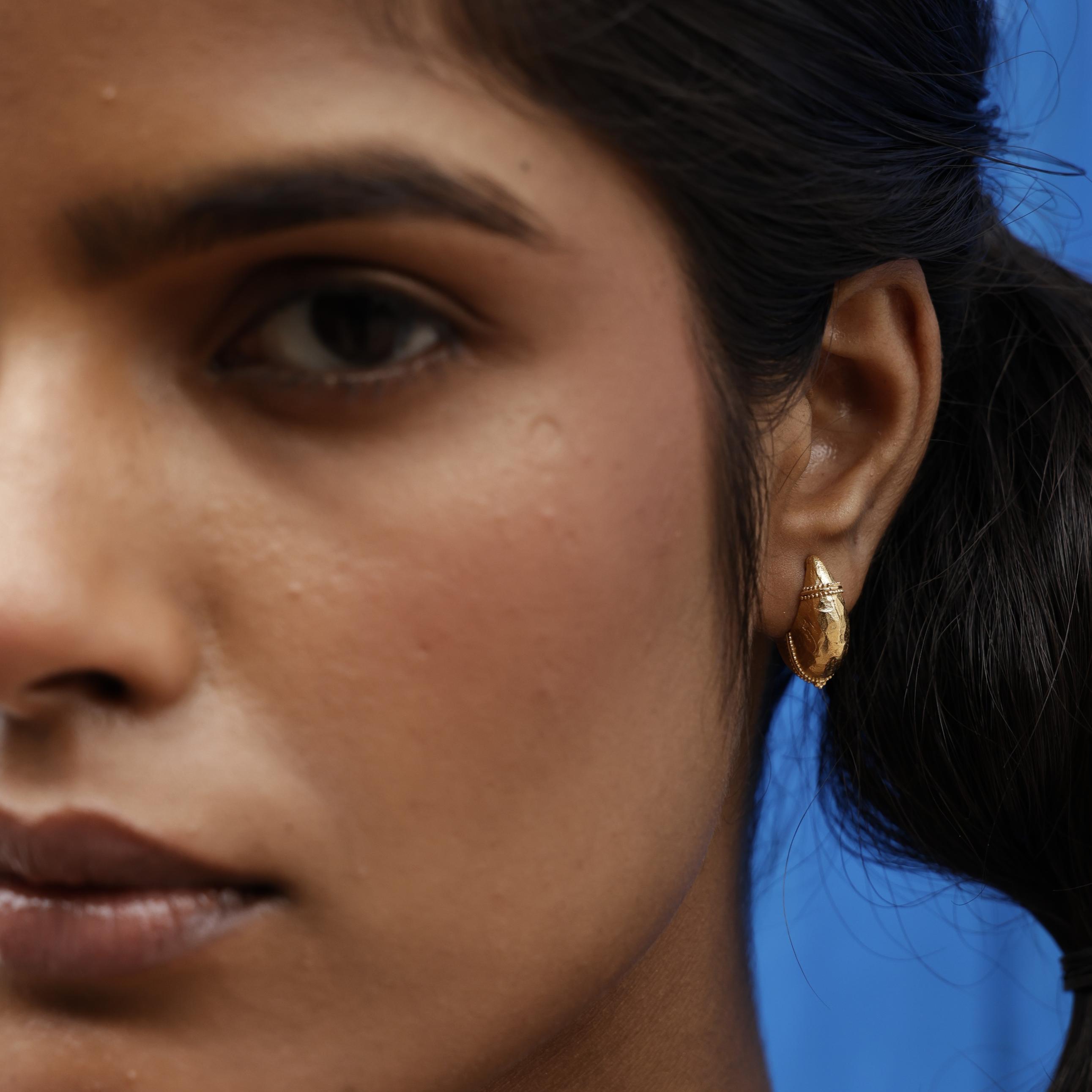 Close-up of a person wearing a gold dome hoop earring with a blue background