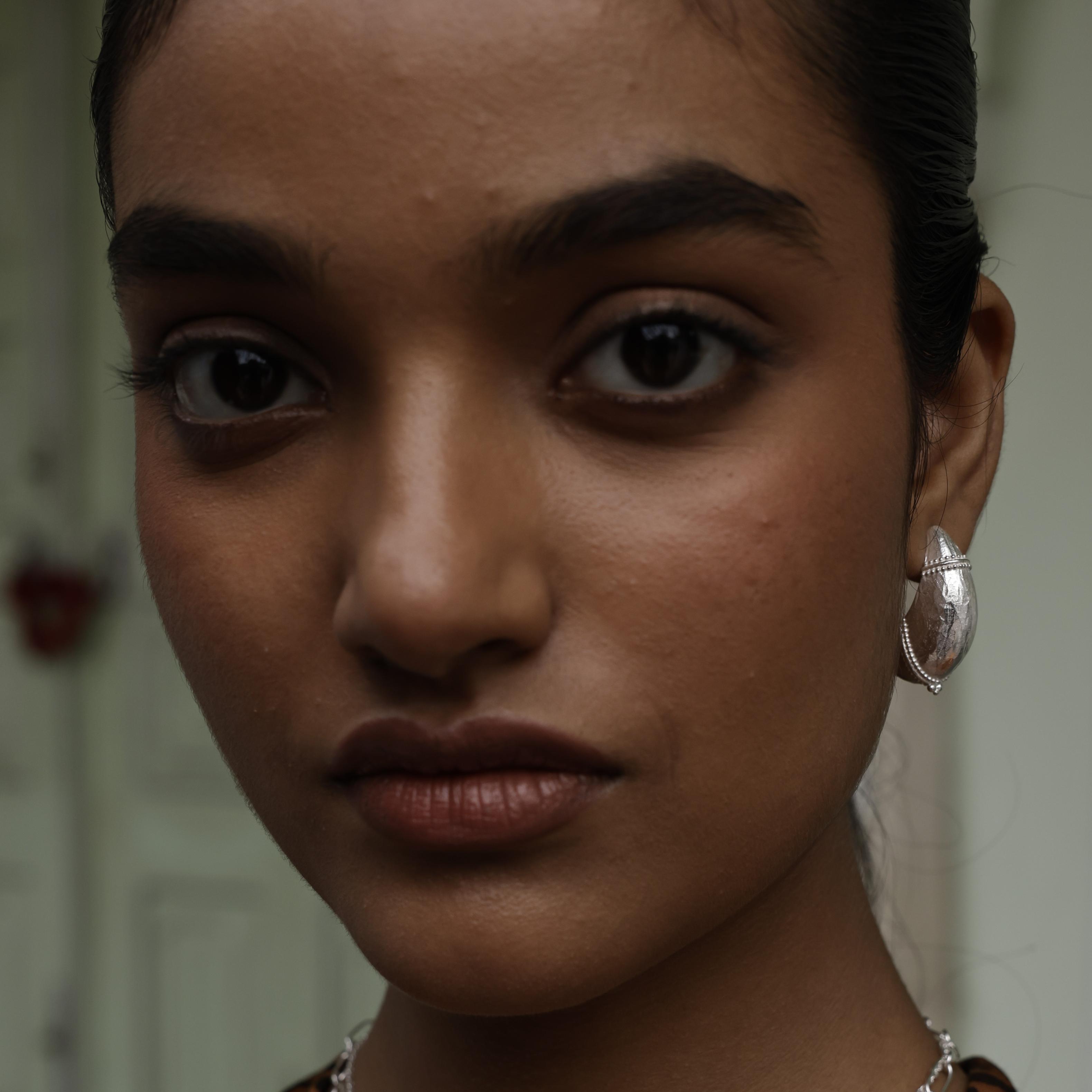 Close-up of a woman wearing silver dome crescent hoop earrings with a blurred background