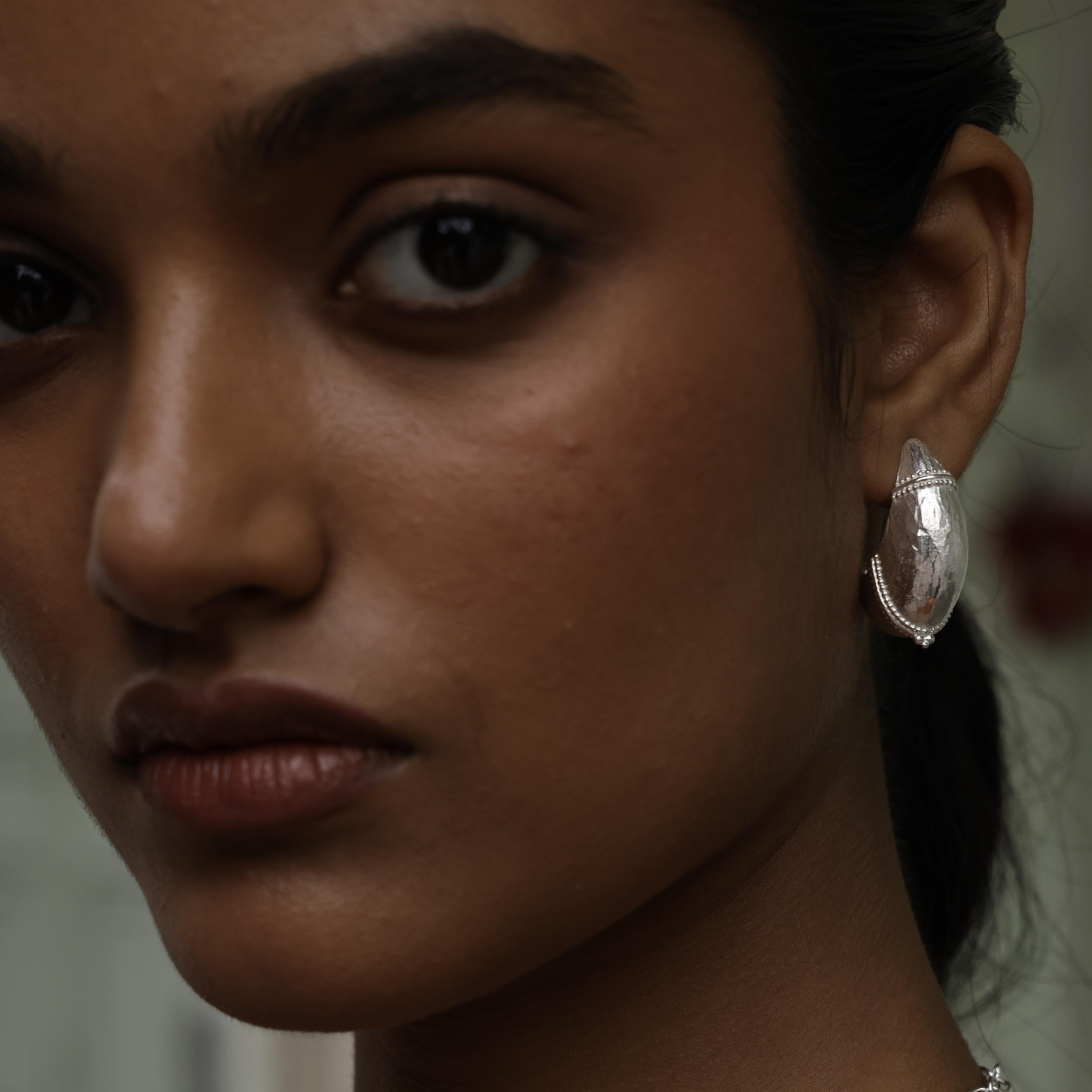 Close-up of a woman wearing a silver  domed hoop earring with intricate design.