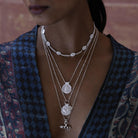 Close-up of a person wearing multiple silver necklaces and talismans with intricate designs.