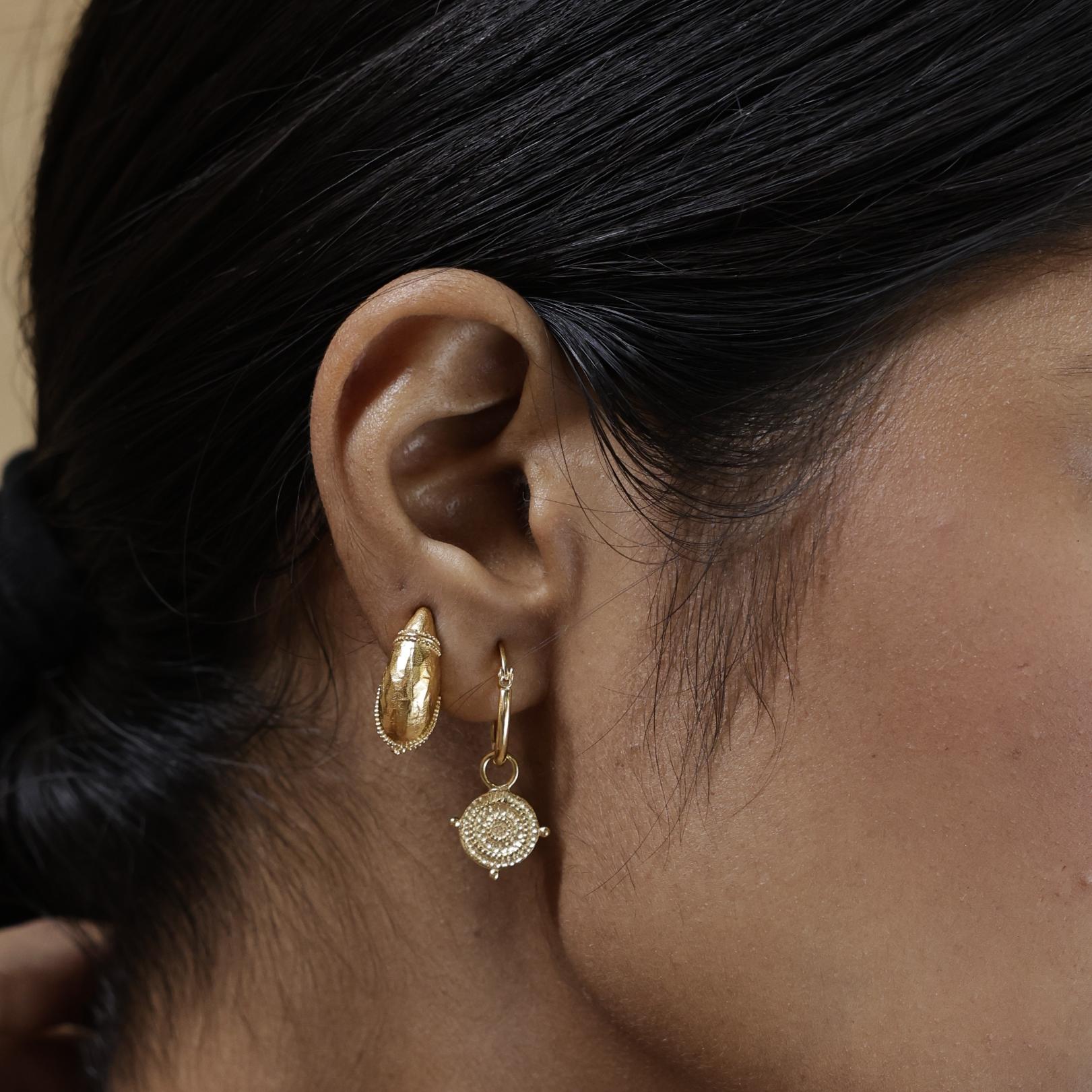 Woman wearing small gold shield hoop earrings layered with Loft & Daughter Mini Dome Earrings