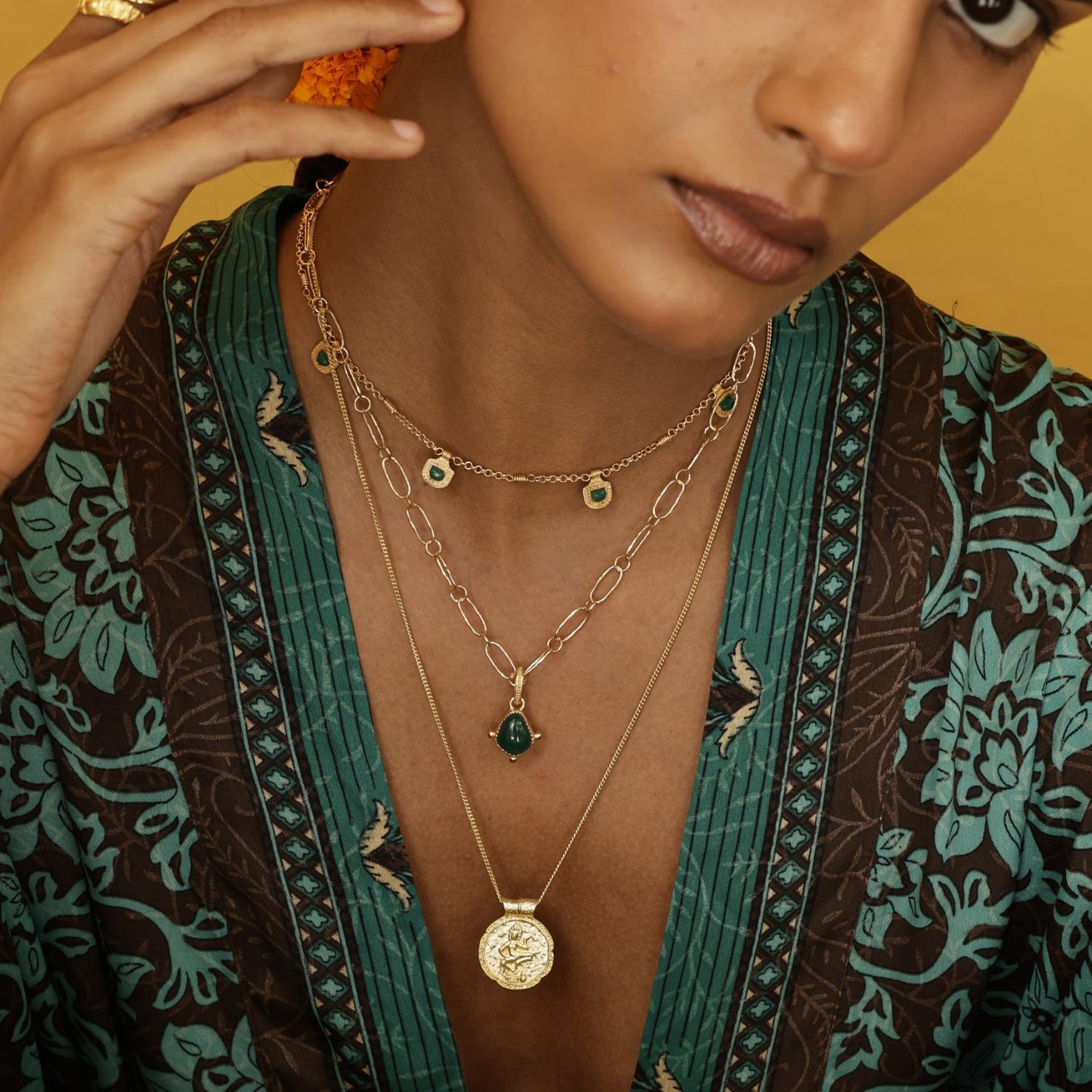 Woman wearing the Forever Young Pendant layered with other gold talismans, symbol of confidence and timeless femininity