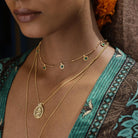 Close-up of a person wearing gold necklaces with green gemstones against a patterned Kimono