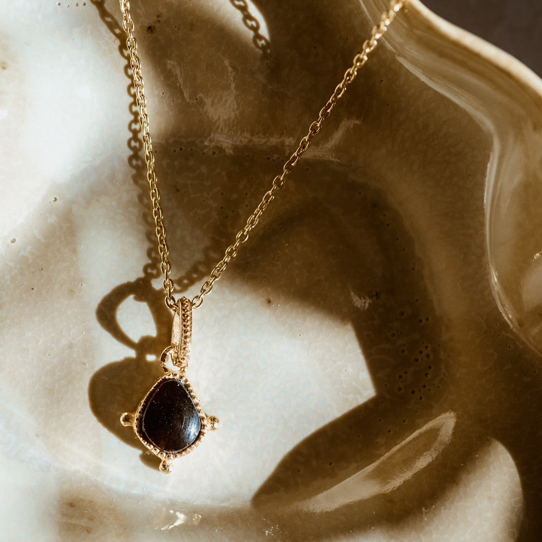 Gold necklace with a red garnet pendant on a textured beige surface