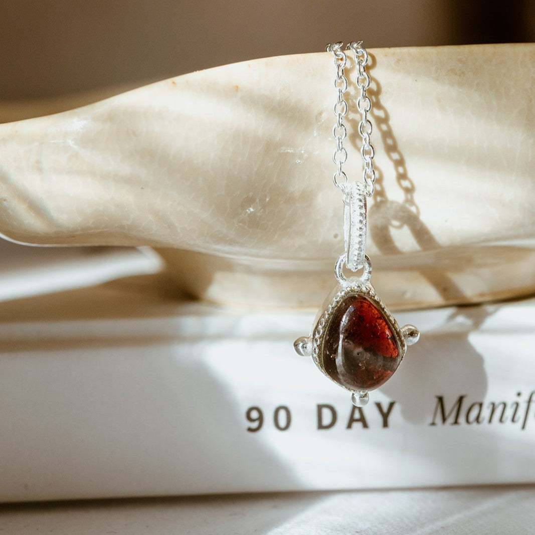 Silver ecklace with a red garnet stone pendant on a marble surface