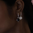 Close-up of an ear wearing a silver shield hoop earring stacked with a gemstone hoop earring