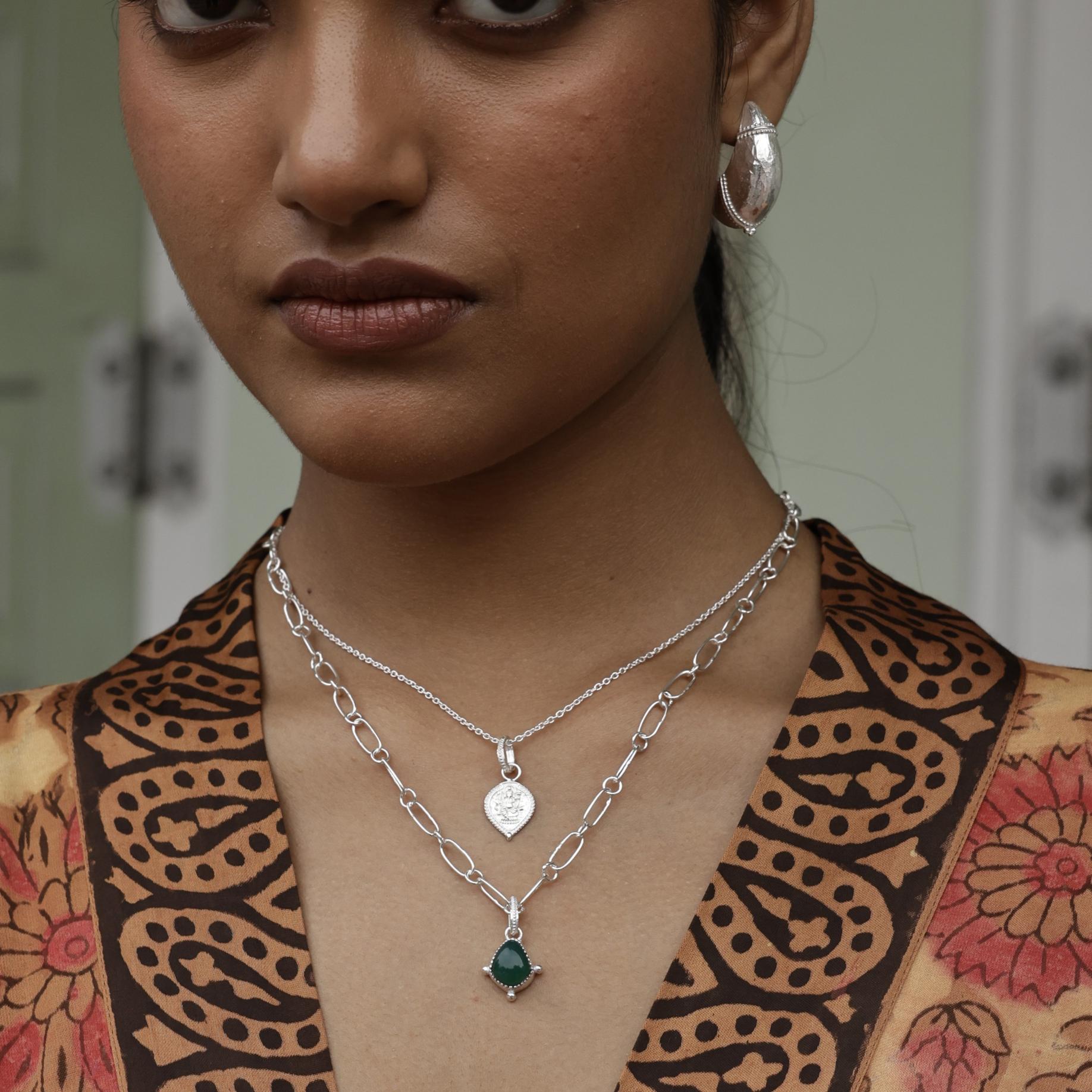 Woman wearing a silver necklace with a garnet pendant, close-up of her neck and upper chest.