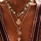 A close-up of a person wearing layered necklaces. The top necklace features green and white beads with a silver toggle clasp.