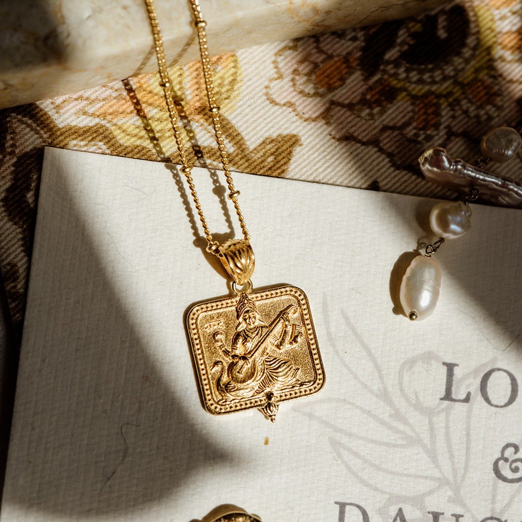 Gold Saraswati pendant necklace styled with a freshwater pearl necklace and patterned fabric