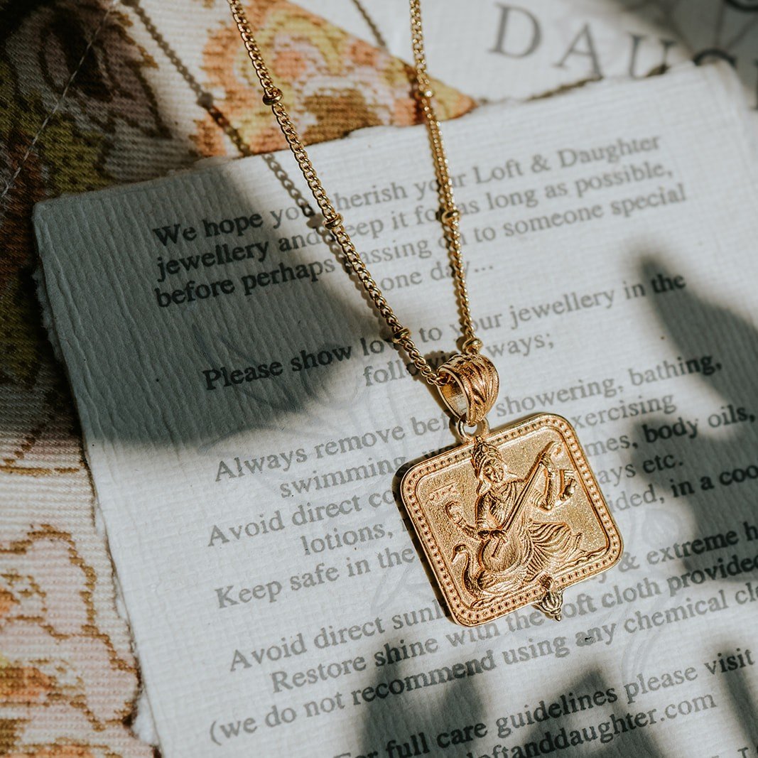 Gold Saraswati pendant necklace draped across a jewellery care card