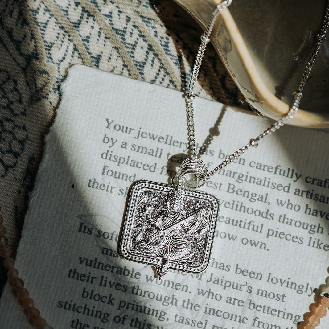 Silver Saraswati pendant necklace styled with a beaded bracelet and patterned fabric